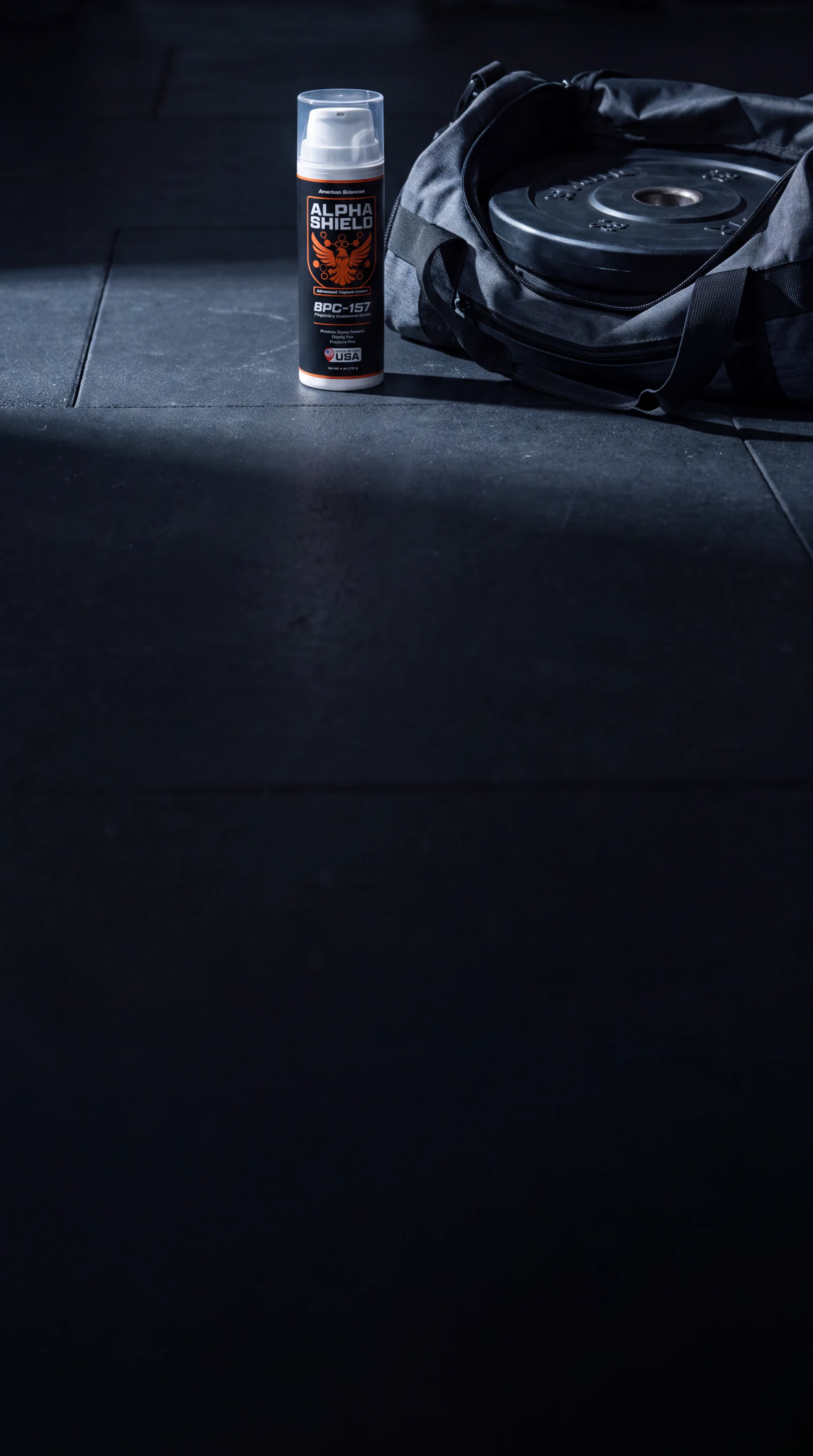 Labelled Alpha Shield bottle beside an open gym bag and a weight plate